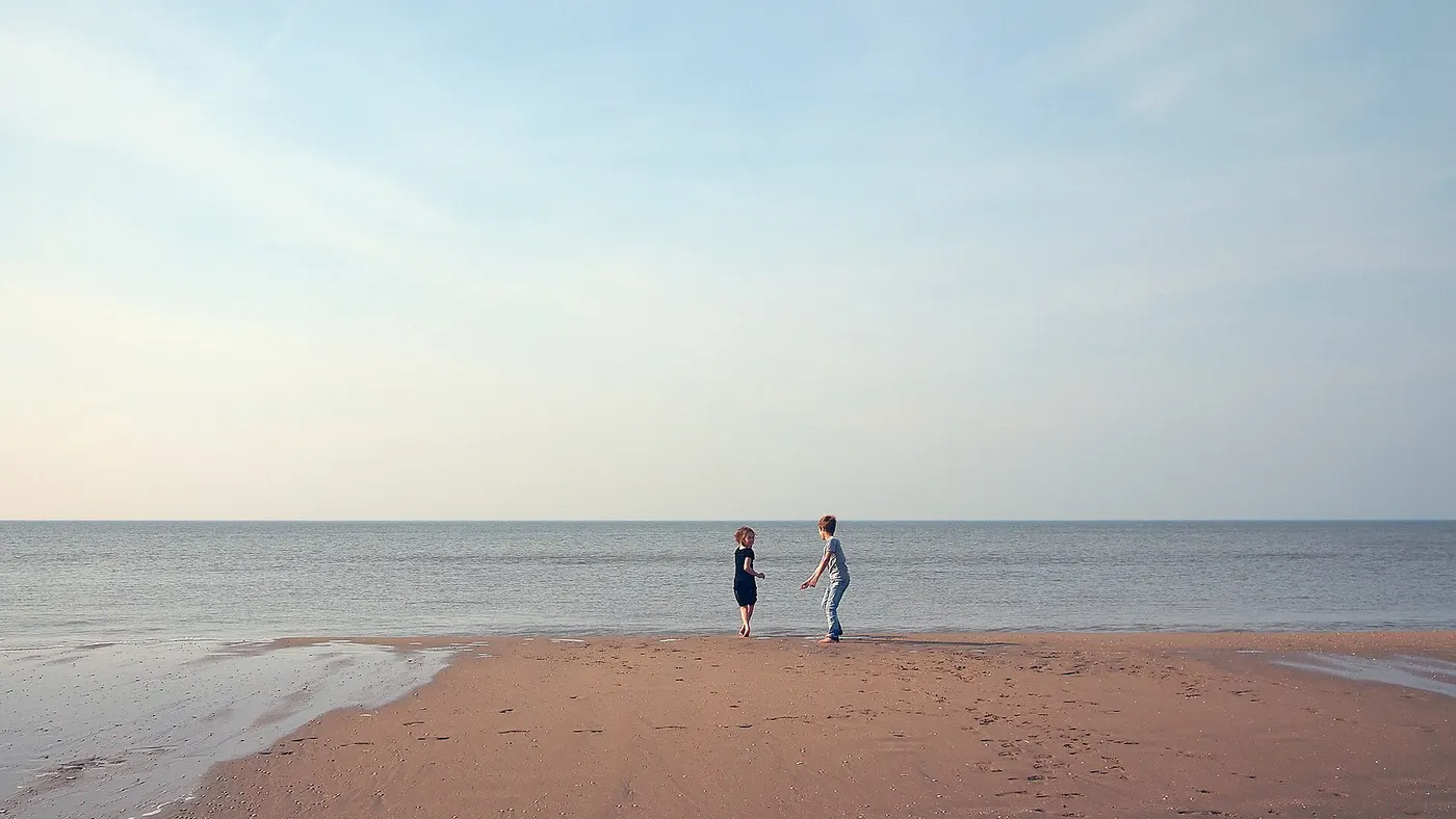 Deux silhouettes au bord de l’eau sur une plage, en été