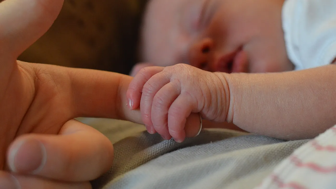 La main d’un bébé endormi serrant le doigt d’un adulte