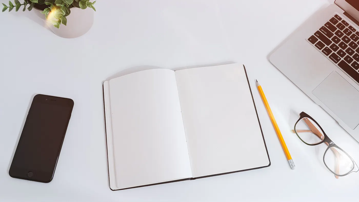 Un carnet ouvert, des lunettes et un crayon posés près d’un ordinateur
