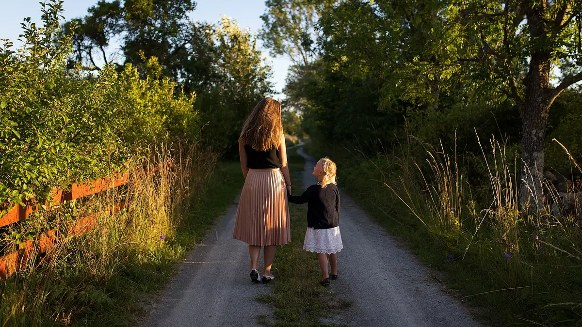 Une mère et son enfant marchant main dans la main sur un chemin de campagne