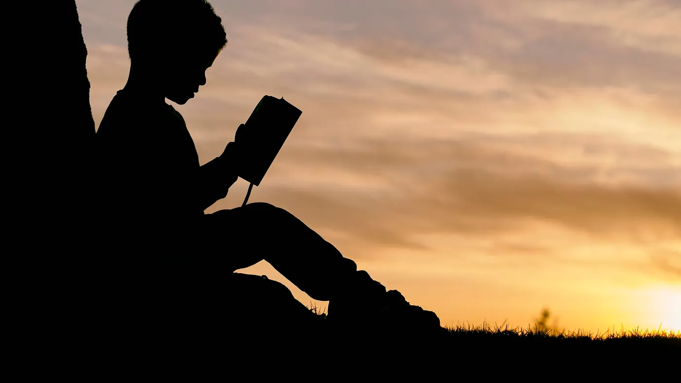 Silhouette d’un enfant qui lit un livre au coucher du soleil