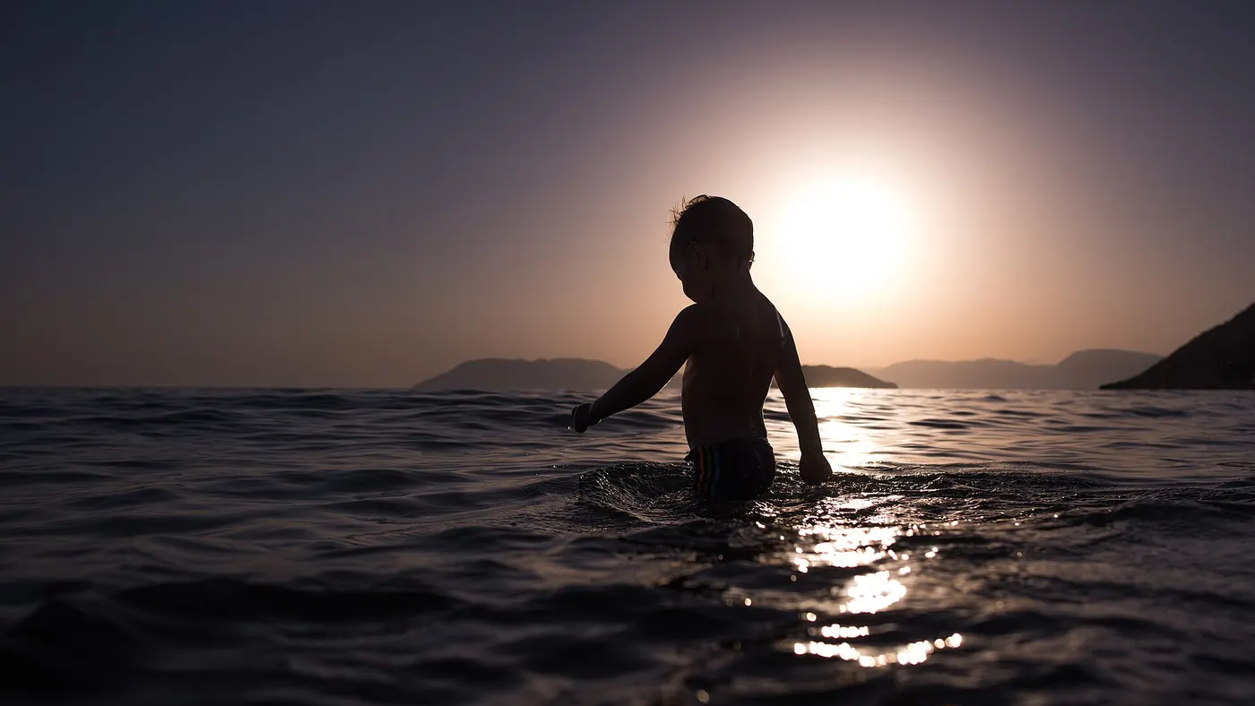 Silhouette d’un enfant immobile dans l’eau au soleil couchant