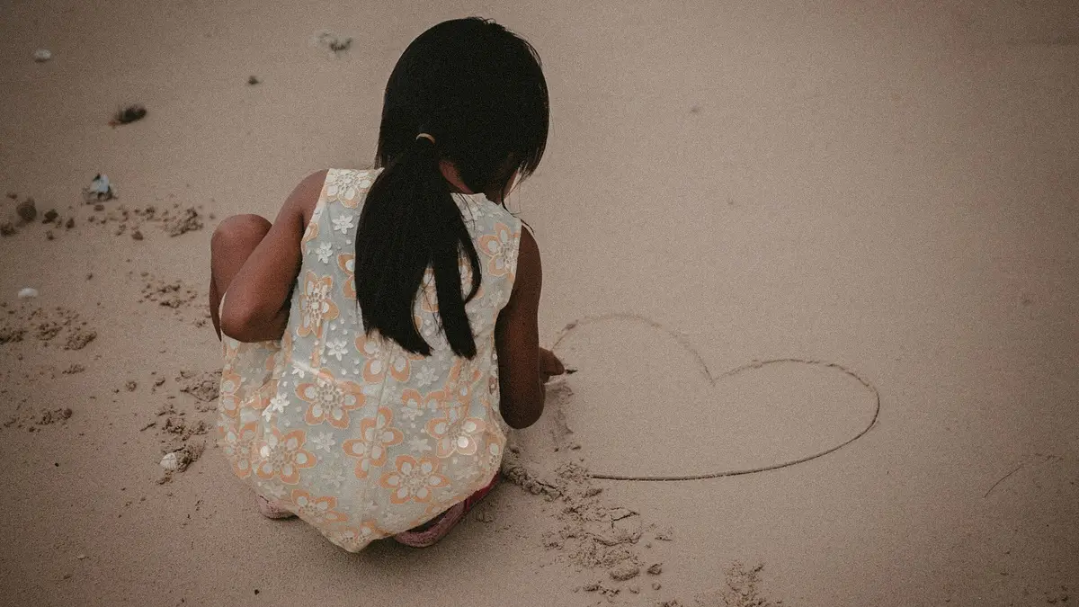 Une fillette qui dessine un cœur dans le sable