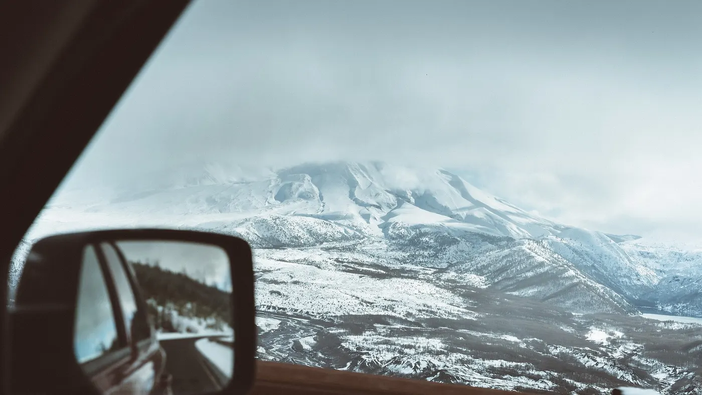 Des montagnes enneigées vues dans le rétroviseur d’une voiture